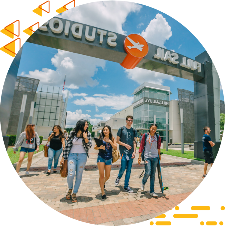 Four students casually chatting and walking under the Full Sail Studios archway, a blue sky with clouds in the background.